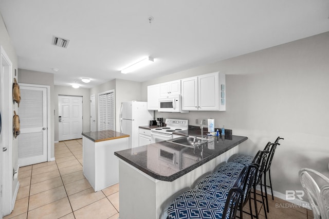 kitchen featuring white appliances, light tile patterned floors, a breakfast bar, kitchen peninsula, and sink