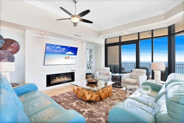 living room featuring a ceiling fan, a glass covered fireplace, and crown molding