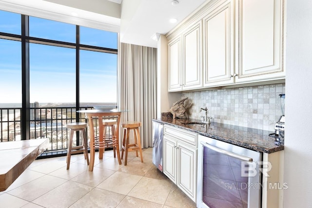 kitchen with beverage cooler, dark stone counters, a sink, expansive windows, and backsplash