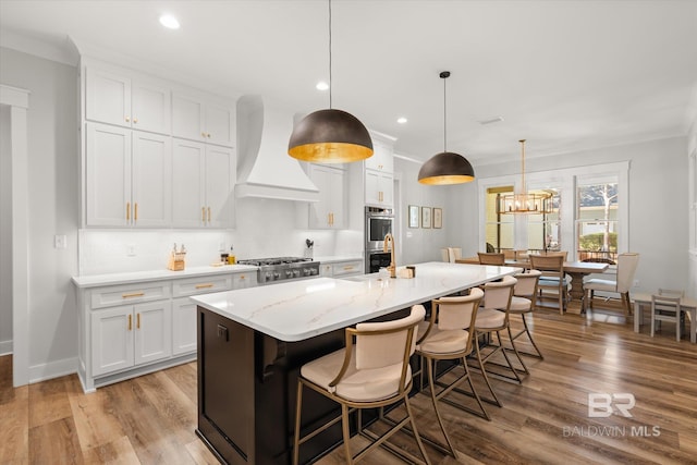 kitchen with custom exhaust hood, appliances with stainless steel finishes, a center island with sink, and white cabinetry