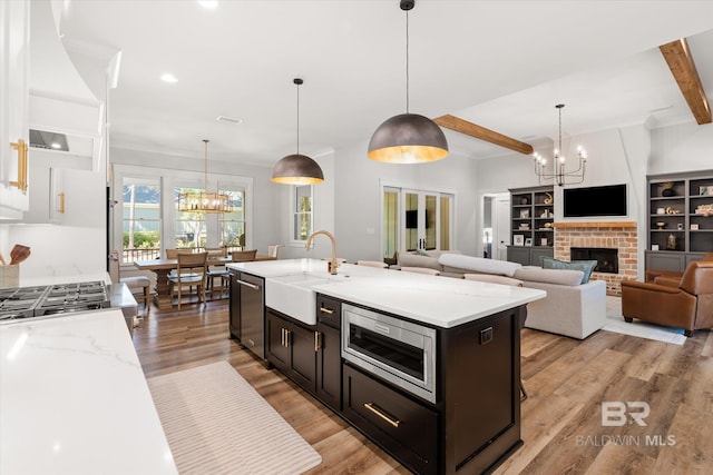 kitchen with beamed ceiling, light wood-style flooring, a notable chandelier, stainless steel appliances, and a sink