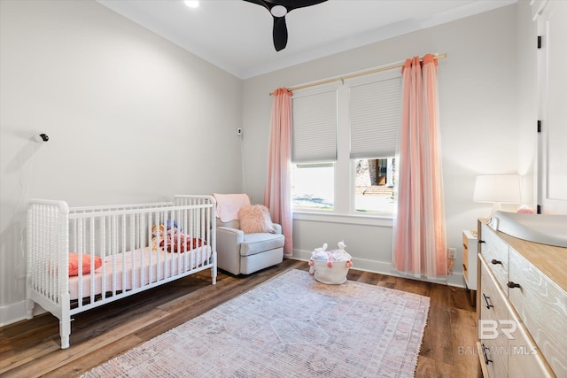 bedroom with a crib, wood finished floors, baseboards, and a ceiling fan