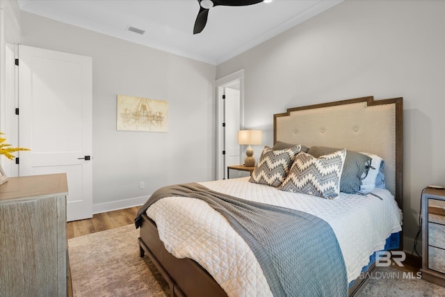 bedroom with wood finished floors, visible vents, baseboards, ceiling fan, and crown molding