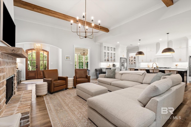 living area featuring an inviting chandelier, beamed ceiling, wood finished floors, and arched walkways