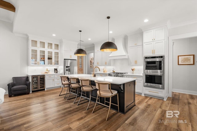 kitchen featuring beverage cooler, premium range hood, stainless steel appliances, light countertops, and a kitchen breakfast bar