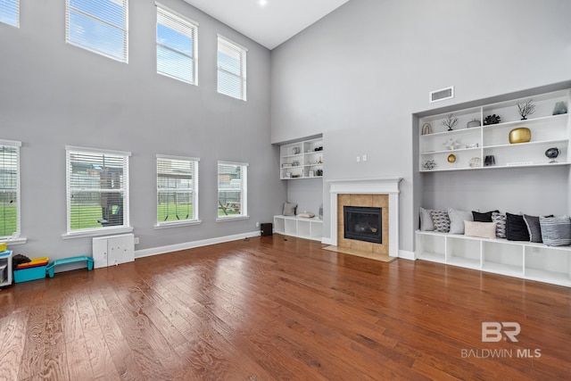 unfurnished living room with a tile fireplace, wood-type flooring, a high ceiling, and built in shelves