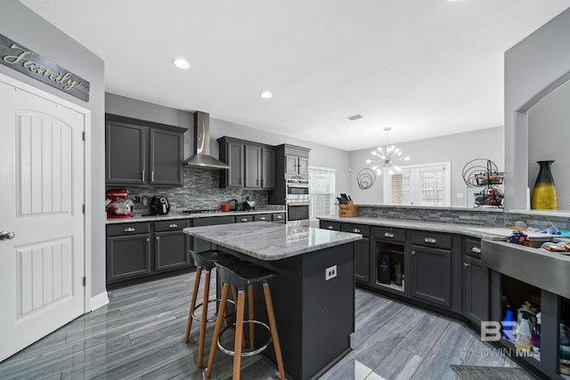 kitchen featuring pendant lighting, backsplash, a kitchen breakfast bar, a center island, and wall chimney exhaust hood