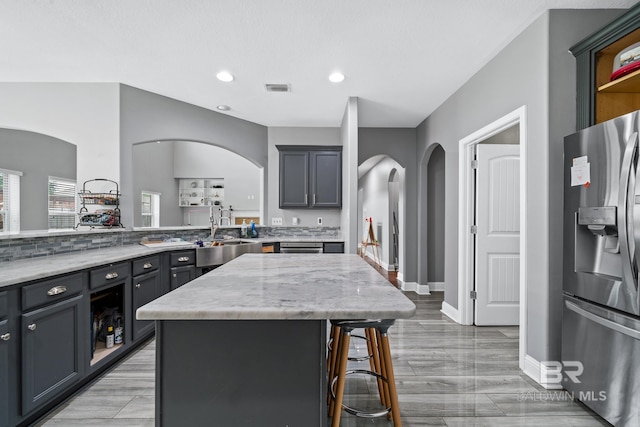 kitchen with sink, a breakfast bar area, a center island, stainless steel refrigerator with ice dispenser, and light stone countertops