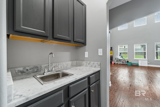 kitchen featuring sink, gray cabinetry, dark hardwood / wood-style floors, a high ceiling, and light stone countertops