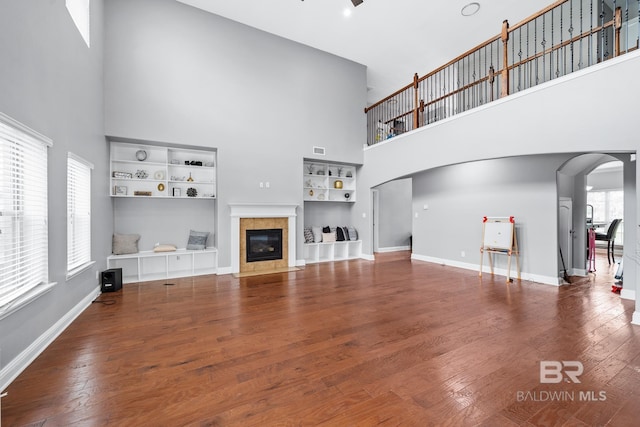 unfurnished living room featuring hardwood / wood-style flooring, a fireplace, built in shelves, and a towering ceiling