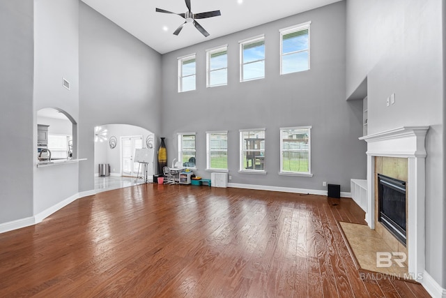 unfurnished living room featuring ceiling fan, plenty of natural light, a tiled fireplace, and hardwood / wood-style floors