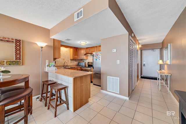 kitchen featuring sink, tasteful backsplash, kitchen peninsula, a breakfast bar area, and appliances with stainless steel finishes