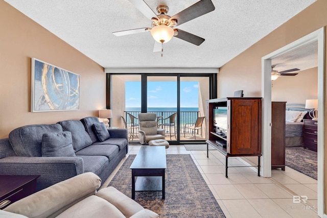 living room featuring ceiling fan, light tile patterned floors, a textured ceiling, and a wall of windows