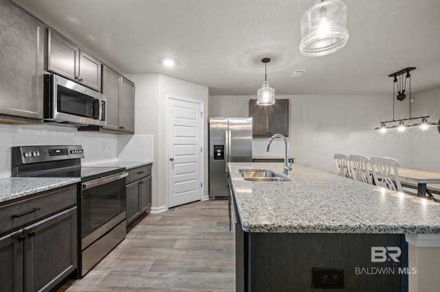 kitchen with appliances with stainless steel finishes, a center island with sink, light hardwood / wood-style flooring, and sink