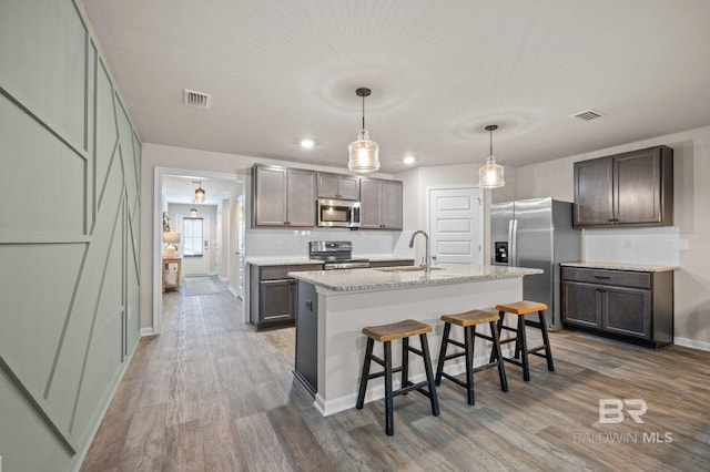 kitchen featuring pendant lighting, a center island with sink, sink, hardwood / wood-style flooring, and stainless steel appliances