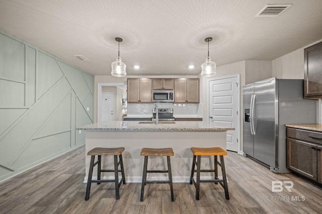 kitchen featuring pendant lighting, a center island with sink, sink, light hardwood / wood-style flooring, and stainless steel appliances