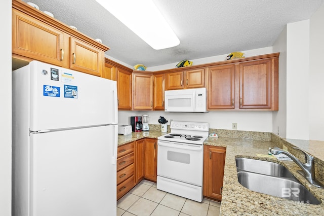 kitchen with light stone counters, light tile patterned floors, a sink, a textured ceiling, and white appliances