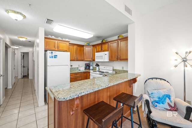 kitchen with a peninsula, white appliances, brown cabinetry, and visible vents