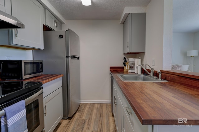 kitchen with a textured ceiling, light hardwood / wood-style flooring, appliances with stainless steel finishes, sink, and butcher block counters