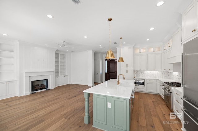 kitchen with high end appliances, a kitchen island with sink, ceiling fan, pendant lighting, and white cabinets