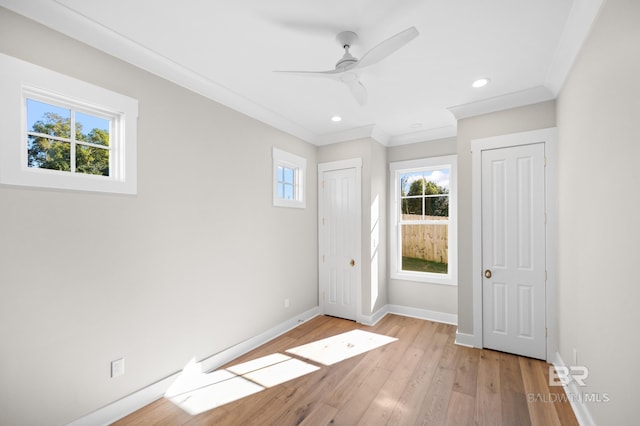 unfurnished bedroom featuring multiple windows, light wood-type flooring, ceiling fan, and ornamental molding