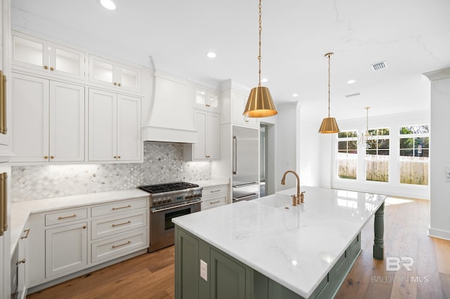 kitchen with custom range hood, pendant lighting, a center island with sink, high quality appliances, and white cabinetry