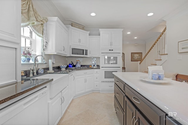 kitchen with crown molding, white appliances, white cabinets, and a sink