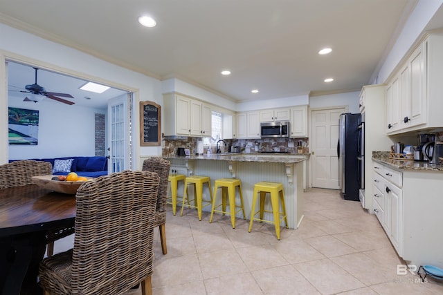 kitchen with white cabinets, appliances with stainless steel finishes, decorative backsplash, and a breakfast bar area