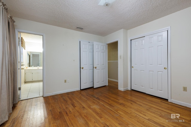 unfurnished bedroom featuring ensuite bath, a textured ceiling, and wood-type flooring