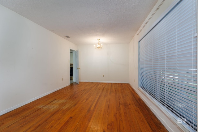 spare room with a notable chandelier, wood-type flooring, and a textured ceiling