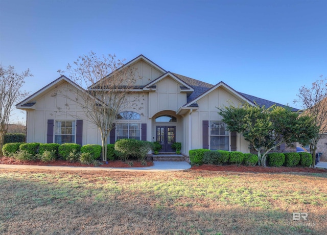 view of front of property with board and batten siding, french doors, a front lawn, and roof with shingles