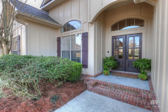 view of exterior entry featuring french doors, board and batten siding, and a shingled roof