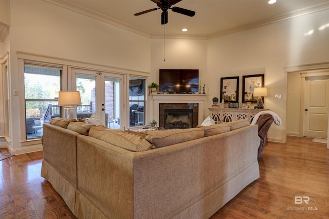 living room with ornamental molding, wood finished floors, a high end fireplace, a high ceiling, and baseboards