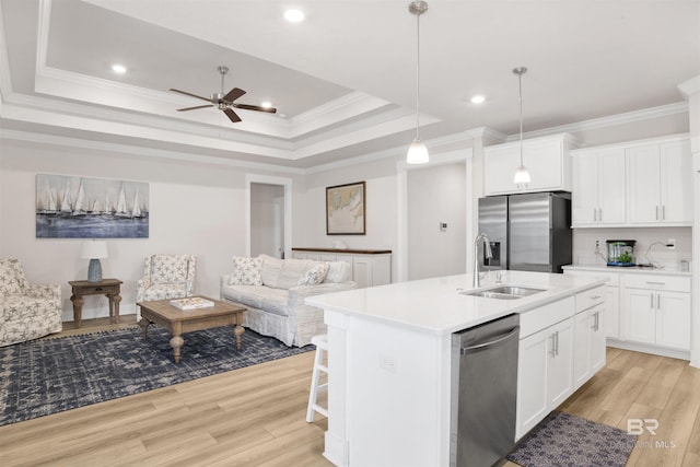 kitchen featuring light wood finished floors, stainless steel appliances, a raised ceiling, open floor plan, and a sink