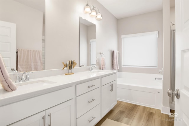 full bath featuring a garden tub, double vanity, wood finished floors, and a sink