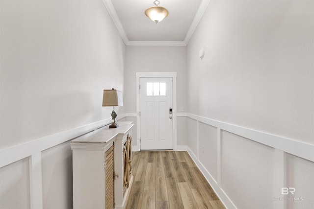 doorway with light wood finished floors, crown molding, and wainscoting