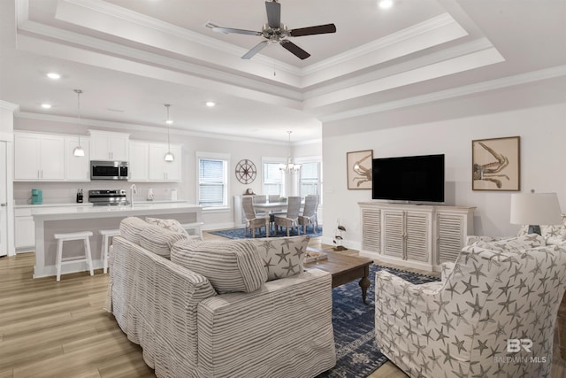 living room featuring light wood-style flooring, a tray ceiling, and ornamental molding