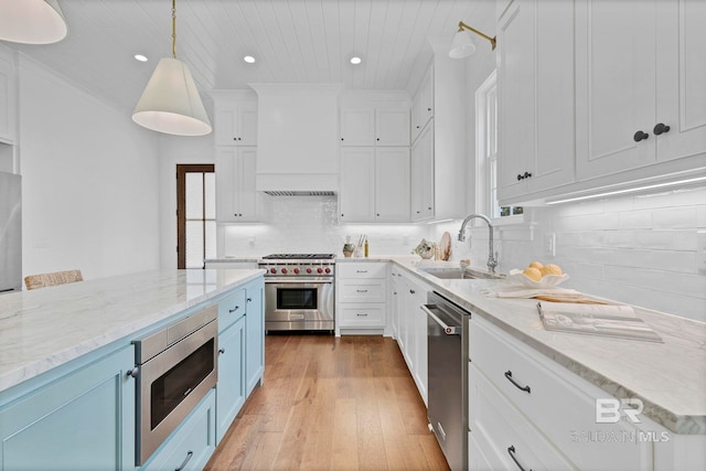 kitchen featuring appliances with stainless steel finishes, blue cabinetry, premium range hood, white cabinetry, and a sink