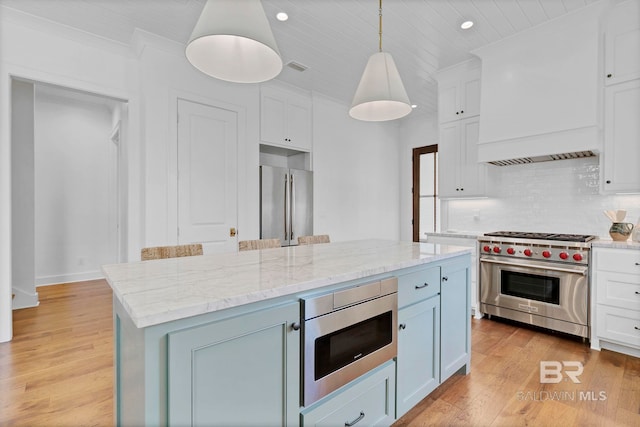 kitchen featuring light wood finished floors, decorative backsplash, appliances with stainless steel finishes, custom exhaust hood, and white cabinetry