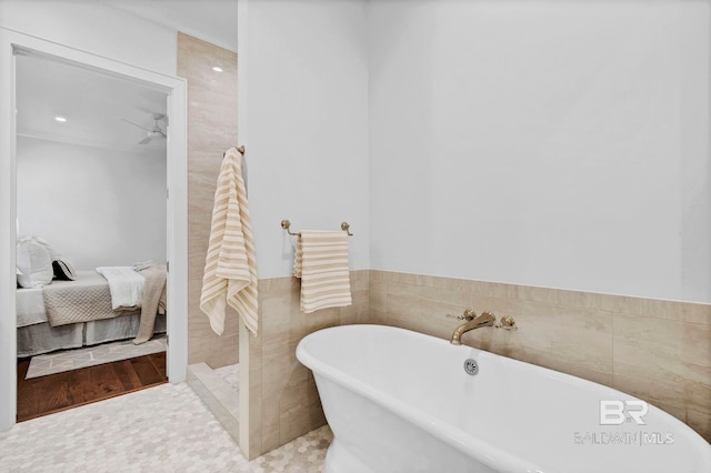 ensuite bathroom with a wainscoted wall, tile walls, a soaking tub, ensuite bathroom, and a ceiling fan