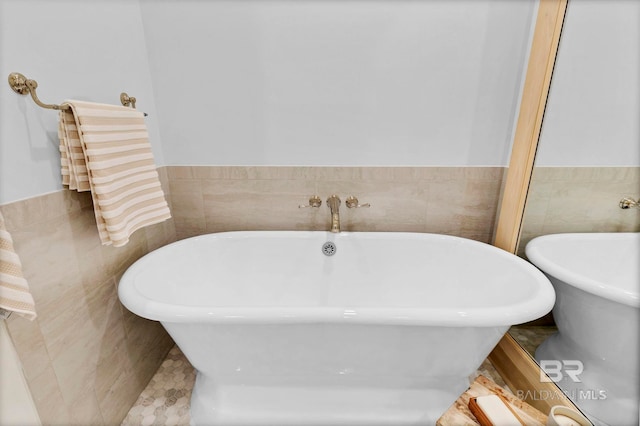 bathroom with a wainscoted wall, tile walls, and a freestanding bath