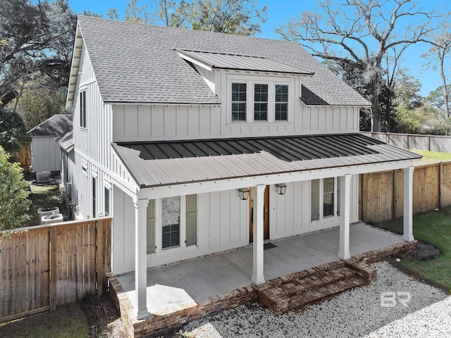 rear view of house with a fenced backyard, roof with shingles, board and batten siding, a standing seam roof, and a patio area