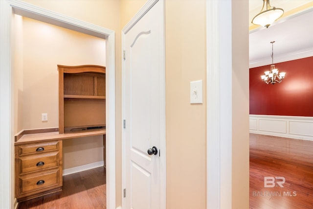 hallway with ornamental molding, an inviting chandelier, and hardwood / wood-style floors