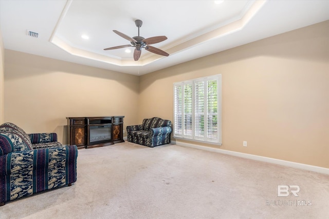 living area with ornamental molding, light colored carpet, ceiling fan, and a raised ceiling