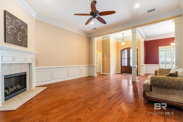 living room featuring crown molding, decorative columns, a tiled fireplace, and light hardwood / wood-style flooring