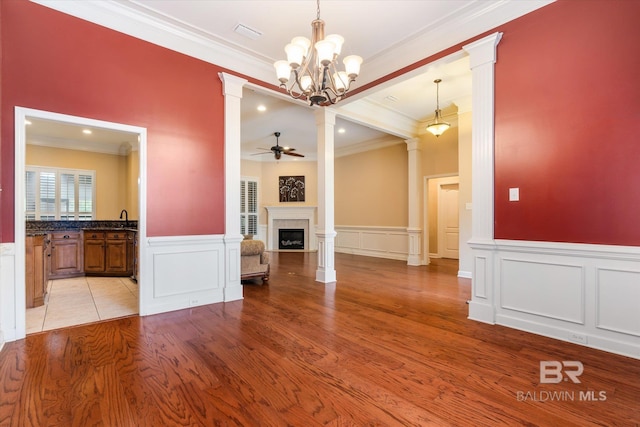 unfurnished living room featuring light wood-type flooring, crown molding, and ornate columns