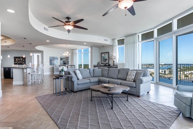 tiled living room featuring a tray ceiling and ceiling fan with notable chandelier