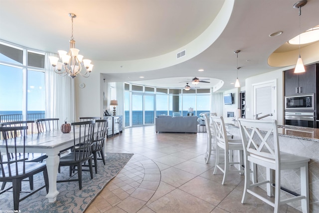 tiled dining space featuring floor to ceiling windows, a water view, a tray ceiling, and ceiling fan with notable chandelier