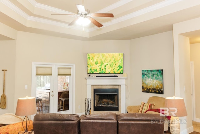 living room featuring ceiling fan, a raised ceiling, french doors, a tiled fireplace, and crown molding