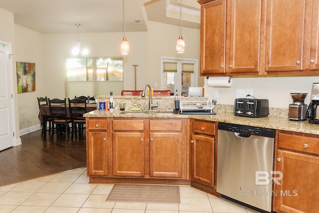 kitchen featuring light wood-type flooring, hanging light fixtures, sink, stainless steel dishwasher, and light stone countertops